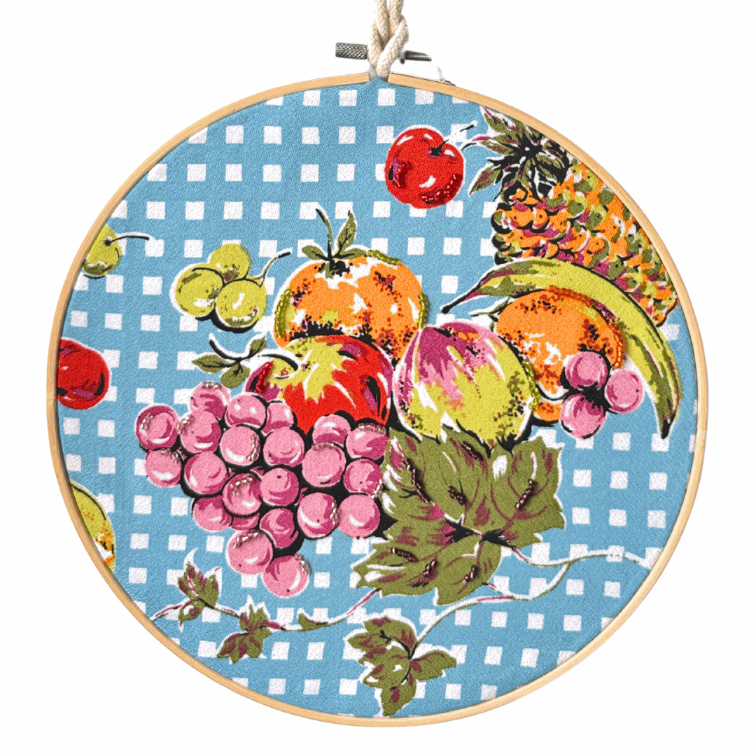 Retro kitchen fruit bowl framed in bamboo hoop with beaded vintage tea towel design hanging on wall