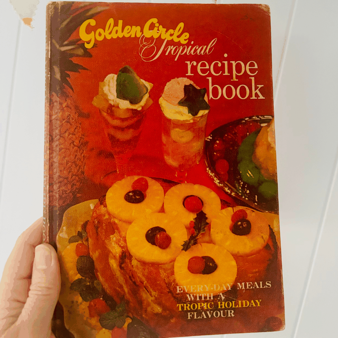 Vintage 'Golden Circle Tropical Recipe Book' held by a hand on a white background