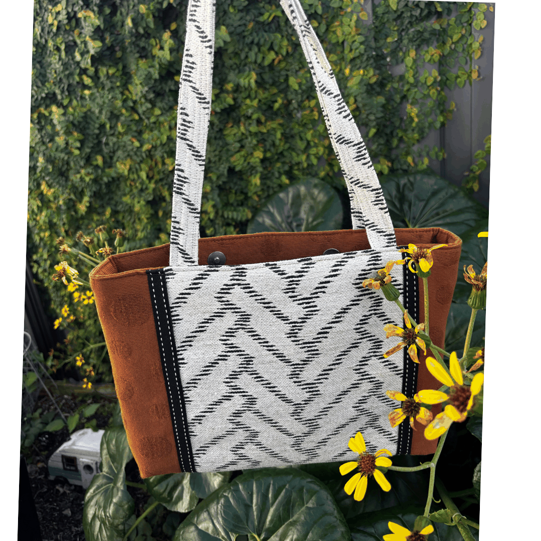 Burnt Caramel Noir handcrafted shoulder bag held in natural light with yellow flowers – Japanese cotton/linen with panel detail – Lyssy May