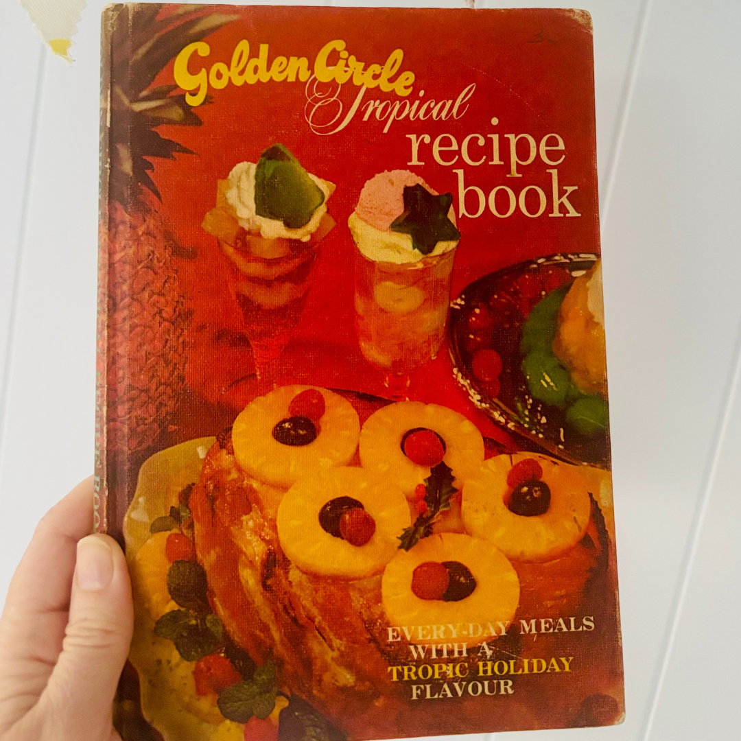 Vintage 'Golden Circle Tropical Recipe Book' held by a hand on a white background