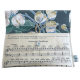 Handmade sheet music wallet open to show deep blue floral wallpaper lining with magnetic clasp, featuring Pattering Raindrops piano music on the front