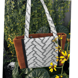 Burnt Caramel Noir handcrafted shoulder bag held in natural light with yellow flowers – Japanese cotton/linen with panel detail – Lyssy May