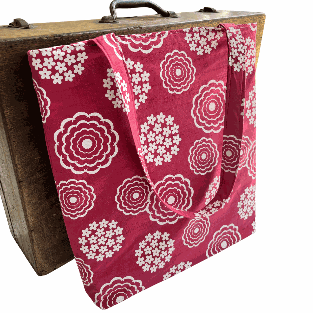 Pink tote bag with white floral pattern draped over a wooden suitcase.