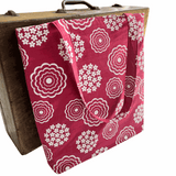 Pink tote bag with white floral pattern draped over a wooden suitcase.
